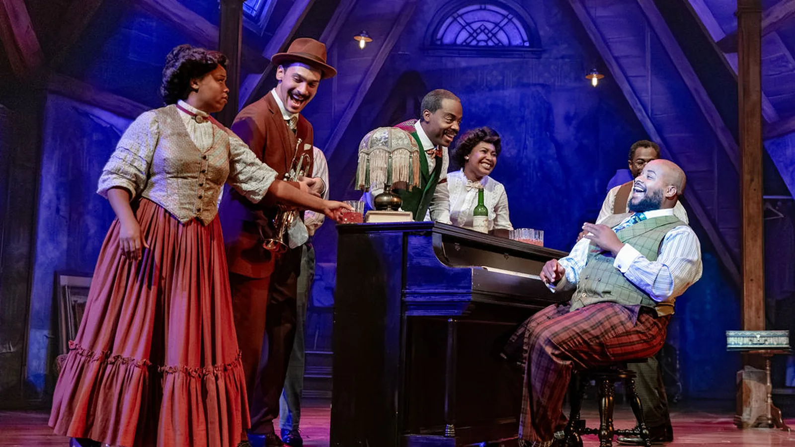 Three Ragtime performers on stage in period costume, with a woman in a feathered hat in front.