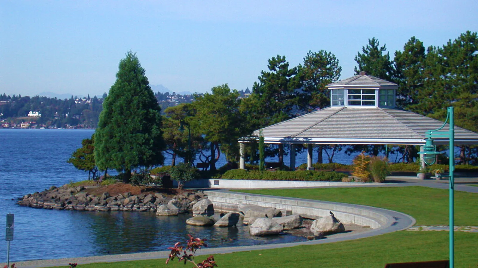 The open pavilion at Marina Park in Kirkland, with a curved roof, lawn, and Lake Washington behind it.